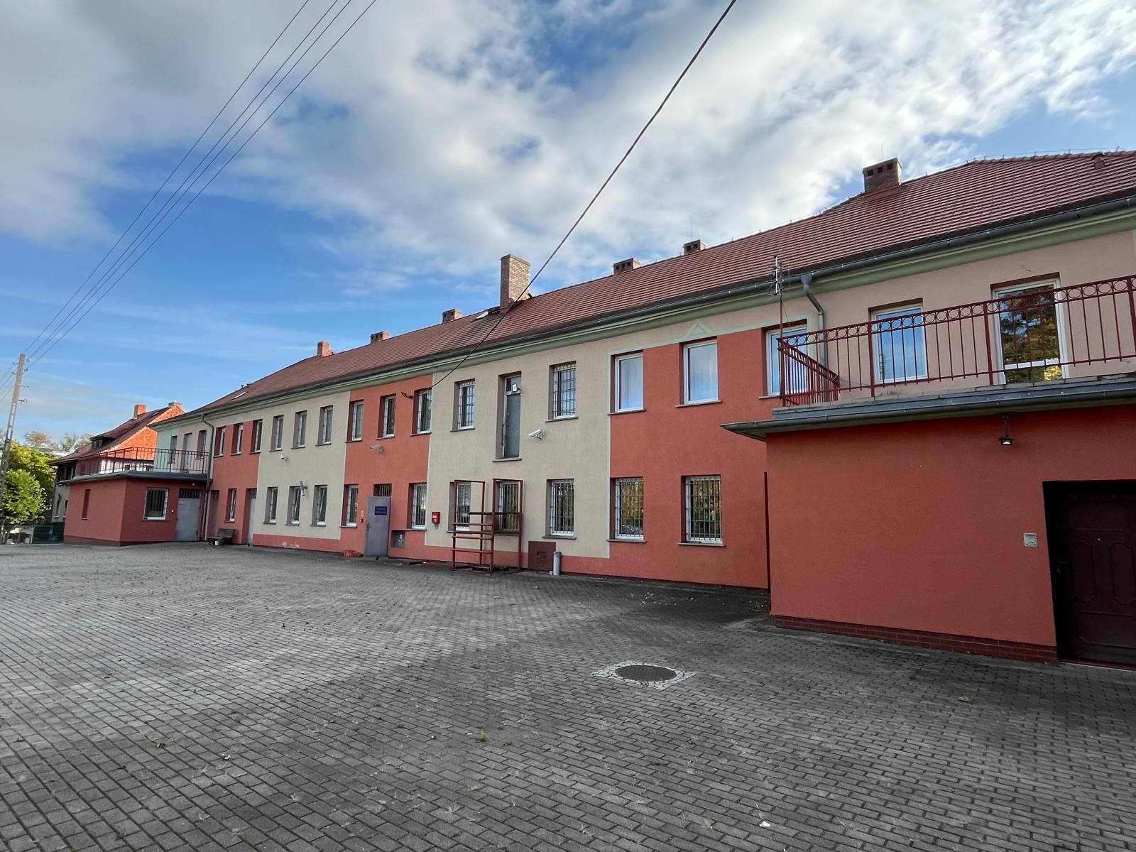 Budynek jednopiętrowy z kolorową elewacją. Widok na parking przy budynku.