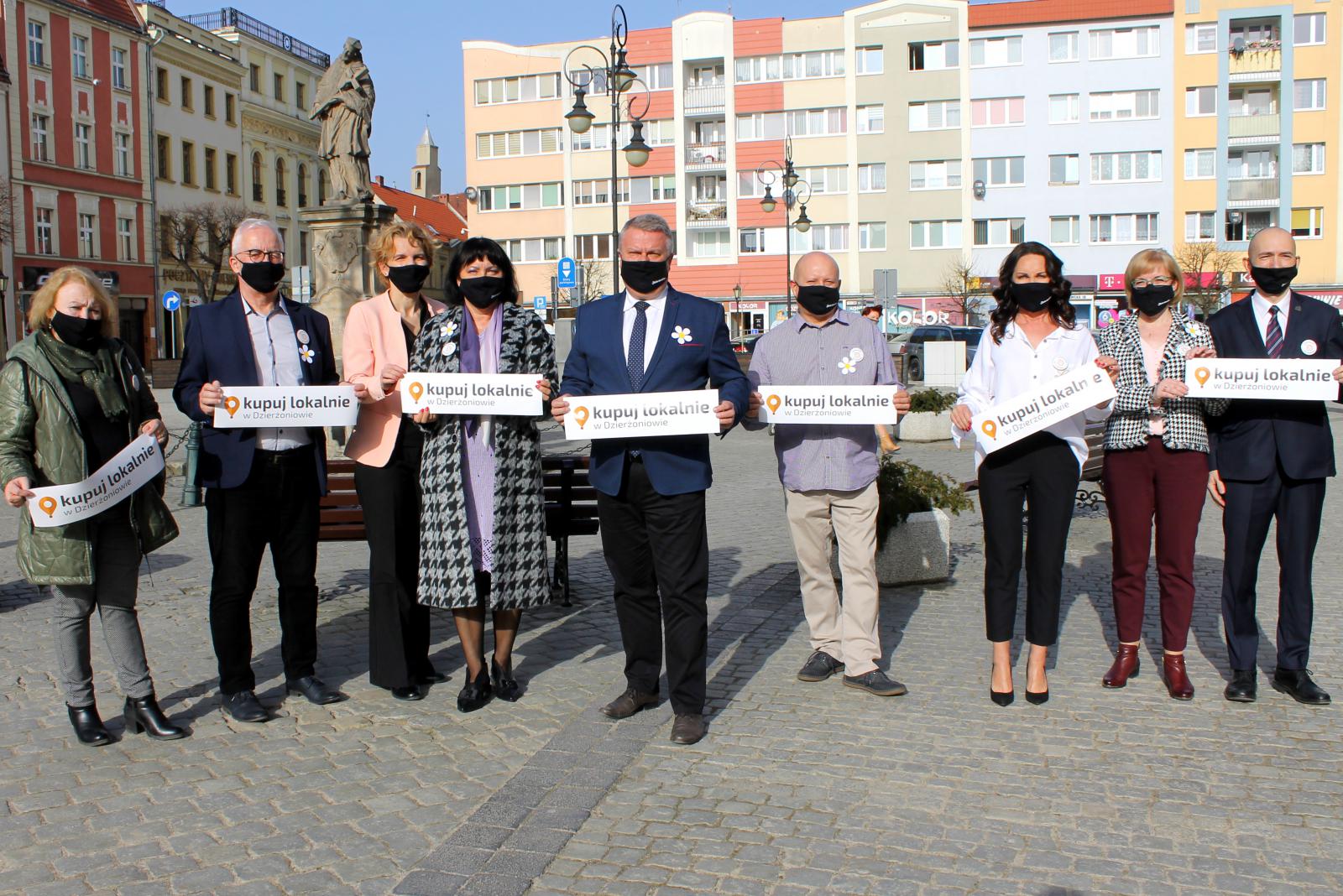 Burmistrz oraz przedstawiciele Dzierżoniowskiej Rady Przedsiebiorców na dzierżoniowskim rynku trzymają naklejki z logo kampanii Kupuj Loklanie w Dzierżoniowie