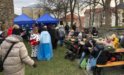 Ludzie siedzący przy stołach, po bokach kamienne, zabytkowe mury obronne Ludzie siedzą przy stołach, po bokach kamienne, zabytkowe mury obronne.