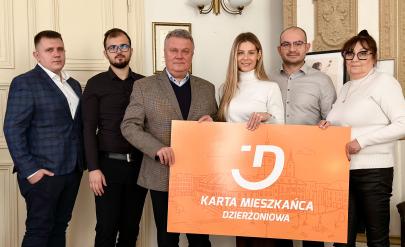 Burmistrz i lokalni przedsiębiorcy pozują do zdjęcia w gabinecie burmistrza z planszą „Karta Mieszkańca Dzierżoniowa"