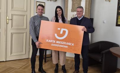 Trzy osoby trzymają planszę z napisem „Karta Mieszkańca Dzierżoniowa”