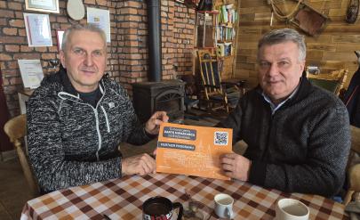 Dwóch mężczyzn przy stoliku trzyma naklejkę "Partner Programu. Tu honorujemy Kartę Mieszkańca Dzierżoniowa"