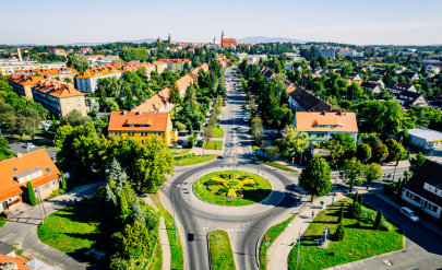 Panorama Dzierżoniowa z lotu ptaka – rondo na pierwszym planie, zabudowa miejska otoczona zielenią oraz widok na centrum miasta i wzgórza w oddali.