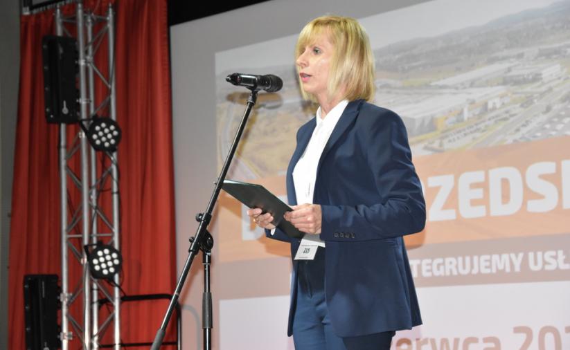 Kobieta stoi na scenie i przemawia do mikrofonu