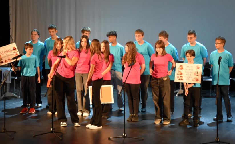 Grupa uczniów stoi na scenie z transparentami 