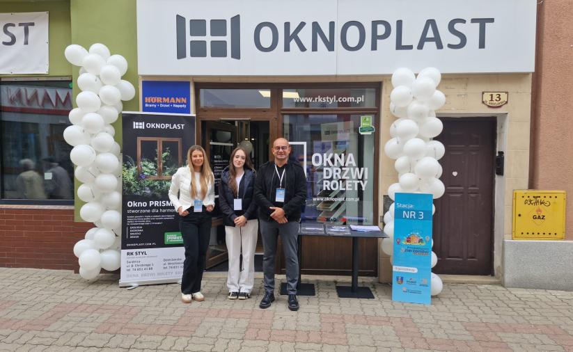 Dwie kobiety i mężczyzna stoją przed siedzibą firmy Oknoplast. Z lewej strony balony i rollup a z prawej stolik i oznaczenie stacji nr 3.