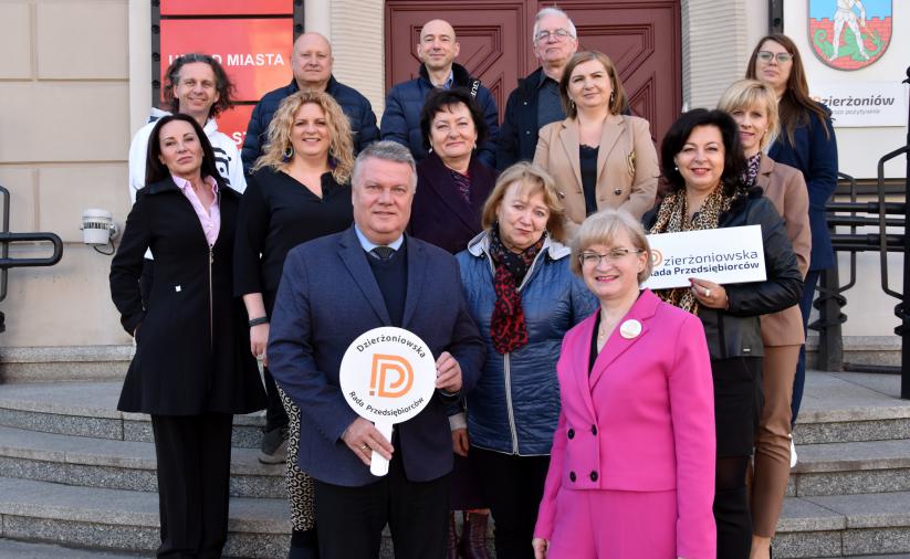 Members of the Dzierżoniów Council of Entrepreneurs are standing on the stairs. The mayor of Dzierżoniów holds a sign in front with the words Council of Entrepreneurs.