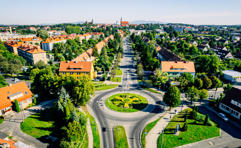 A bird's eye view of Dzierżoniów – a roundabout in the foreground, urban development surrounded by greenery and a view of the city center and hills in the distance.