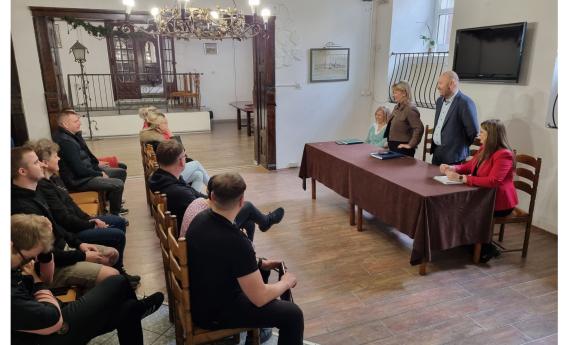 Grupa osób siedzi na krzesłach podczas spotkania.