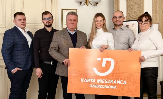Burmistrz i lokalni przedsiębiorcy pozują do zdjęcia w gabinecie burmistrza z planszą „Karta Mieszkańca Dzierżoniowa"