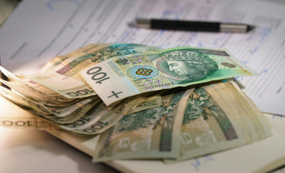 Kilkadziesiąt banknotów stuzłotowych leży na notesie. W tle formularz i długopis. 